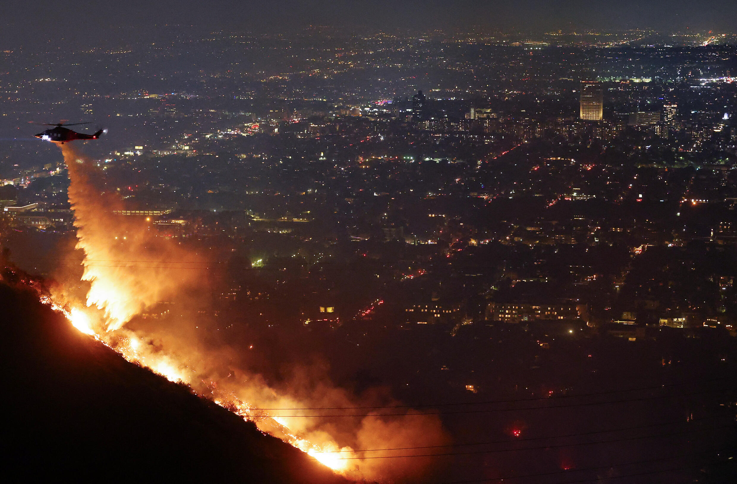 A firefighting helicopter drops water as the Sunset Fire burns in the Hollywood Hills with evacuations ordered on January 8, 2025 in Los Angeles, California.